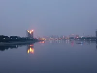 傍晚，我們騎車又來到這里。天色陰暗，整個天空被大霧籠罩，看不到明月與星辰，內心也好似蒙塵。坐了一會兒，已沒有雅興觀賞，往返途中，回頭一望，遠處高樓聳立，樓頂上紅色燈火映在水面上形成一道光束，猶如落日余暉灑在水面上，紅彤彤，金燦燦地，絢爛奪目，水面上依然波光如鏡。驀然心里注入一道光，當你的視覺僅停留在灰色地帶，就難以發現生活的那抹亮色，當你轉念一想，其實好景就在那里，你注意到它，它就給你點亮心情。你看那水，縱然外面煙霧繚繞，我自水波不興，風平浪靜。配圖