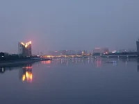 傍晚，我們騎車又來到這里。天色陰暗，整個天空被大霧籠罩，看不到明月與星辰，內心也好似蒙塵。坐了一會兒，已沒有雅興觀賞，往返途中，回頭一望，遠處高樓聳立，樓頂上紅色燈火映在水面上形成一道光束，猶如落日余暉灑在水面上，紅彤彤，金燦燦地，絢爛奪目，水面上依然波光如鏡。驀然心里注入一道光，當你的視覺僅停留在灰色地帶，就難以發現生活的那抹亮色，當你轉念一想，其實好景就在那里，你注意到它，它就給你點亮心情。你看那水，縱然外面煙霧繚繞，我自水波不興，風平浪靜。配圖