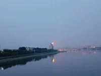 傍晚，我們騎車又來到這里。天色陰暗，整個天空被大霧籠罩，看不到明月與星辰，內心也好似蒙塵。坐了一會兒，已沒有雅興觀賞，往返途中，回頭一望，遠處高樓聳立，樓頂上紅色燈火映在水面上形成一道光束，猶如落日余暉灑在水面上，紅彤彤，金燦燦地，絢爛奪目，水面上依然波光如鏡。驀然心里注入一道光，當你的視覺僅停留在灰色地帶，就難以發現生活的那抹亮色，當你轉念一想，其實好景就在那里，你注意到它，它就給你點亮心情。你看那水，縱然外面煙霧繚繞，我自水波不興，風平浪靜。配圖