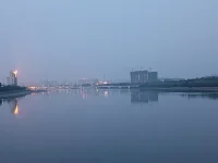 傍晚，我們騎車又來到這里。天色陰暗，整個天空被大霧籠罩，看不到明月與星辰，內心也好似蒙塵。坐了一會兒，已沒有雅興觀賞，往返途中，回頭一望，遠處高樓聳立，樓頂上紅色燈火映在水面上形成一道光束，猶如落日余暉灑在水面上，紅彤彤，金燦燦地，絢爛奪目，水面上依然波光如鏡。驀然心里注入一道光，當你的視覺僅停留在灰色地帶，就難以發現生活的那抹亮色，當你轉念一想，其實好景就在那里，你注意到它，它就給你點亮心情。你看那水，縱然外面煙霧繚繞，我自水波不興，風平浪靜。配圖