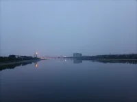 傍晚，我們騎車又來到這里。天色陰暗，整個天空被大霧籠罩，看不到明月與星辰，內心也好似蒙塵。坐了一會兒，已沒有雅興觀賞，往返途中，回頭一望，遠處高樓聳立，樓頂上紅色燈火映在水面上形成一道光束，猶如落日余暉灑在水面上，紅彤彤，金燦燦地，絢爛奪目，水面上依然波光如鏡。驀然心里注入一道光，當你的視覺僅停留在灰色地帶，就難以發現生活的那抹亮色，當你轉念一想，其實好景就在那里，你注意到它，它就給你點亮心情。你看那水，縱然外面煙霧繚繞，我自水波不興，風平浪靜。配圖