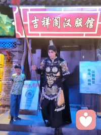 《杨柳青古巷遇戎装赋》
 
暮临津沽杨柳青墟，长街灯华，古肆连楹。余闲步漫游，忽见一戎装少年立巷隅，玄铠鎏纹，长戈倚侧，眉目疏朗，英气凌云。金甲映霓虹，身姿挺拔若青松临风，顾盼之间，俊采飞扬，令人目移心喜。
 
余趋前相与语，言欲留影纪此相逢。少年温雅谦和，闻言欣然颔首，俯仰立坐，皆顺人意，摆姿展态，毫无倦怠，待人以诚，气度温润，初见便觉心头烦扰消解大半。方调镜头之际，一家四口缓步而至，远客夫妻携两稚子，远道来游古镇。夫君执机欲为妻取景，持镜茫然，不知章法。余侧立旁，细教取景光影、身形站位之法，嘱其寻温柔姿态衬佳人风姿。
 
其夫闻言莞尔，回身笑语妻曰：“无妨，可依偎相拥，随心喜乐，不必拘谨。”语罢伸手相挽，妻霎时展颜，笑靥如花，眉眼间羞怯尽散。身旁两童见状，亦拍手嬉闹，绕膝奔走，满是童真烂漫。少顷夫君移步上前，自请立镜前，摹美猴王腾跃之姿，抬手探额，嬉闹无拘，阖家笑语充盈古巷。
 
余立旁静观，心下慨然。此一家四口，夫知惜妻，妻善解意，稚童无忧，彼此体恤成全，无隔阂拘束，方是华夏家庭本真之温情。尘世奔波，世人常困于疏离、苛责，心有郁结，难寻松弛暖意。今古镇灯火、飒爽少年治愈尘俗疲惫，更得此和睦阖家涤荡心绪，恍然知晓治愈本心者，从非远在山海，乃是人间相守的松弛与包容。
 
戎装少年以谦和待人，予过客温柔；寻常夫妇以坦诚相待，予彼此欢愉。烟火古巷，铠甲英姿衬阖家温情，一静一动，皆是人间至善光景。愿九州万户皆如此：夫妻相知不藏拘谨，亲子相伴常存欢颜，家人之间随心抒意，彼此成全，相守和乐，岁岁常有笑语相伴，岁岁皆得温柔治愈。世间万千烦忧，皆可在家人松弛暖意里缓缓消融，人间至幸，莫过于阖家自在，心无芥蒂，喜乐常随。配图