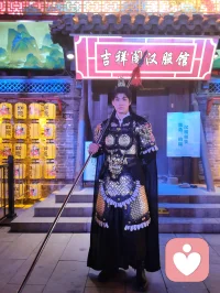 《杨柳青古巷遇戎装赋》
 
暮临津沽杨柳青墟，长街灯华，古肆连楹。余闲步漫游，忽见一戎装少年立巷隅，玄铠鎏纹，长戈倚侧，眉目疏朗，英气凌云。金甲映霓虹，身姿挺拔若青松临风，顾盼之间，俊采飞扬，令人目移心喜。
 
余趋前相与语，言欲留影纪此相逢。少年温雅谦和，闻言欣然颔首，俯仰立坐，皆顺人意，摆姿展态，毫无倦怠，待人以诚，气度温润，初见便觉心头烦扰消解大半。方调镜头之际，一家四口缓步而至，远客夫妻携两稚子，远道来游古镇。夫君执机欲为妻取景，持镜茫然，不知章法。余侧立旁，细教取景光影、身形站位之法，嘱其寻温柔姿态衬佳人风姿。
 
其夫闻言莞尔，回身笑语妻曰：“无妨，可依偎相拥，随心喜乐，不必拘谨。”语罢伸手相挽，妻霎时展颜，笑靥如花，眉眼间羞怯尽散。身旁两童见状，亦拍手嬉闹，绕膝奔走，满是童真烂漫。少顷夫君移步上前，自请立镜前，摹美猴王腾跃之姿，抬手探额，嬉闹无拘，阖家笑语充盈古巷。
 
余立旁静观，心下慨然。此一家四口，夫知惜妻，妻善解意，稚童无忧，彼此体恤成全，无隔阂拘束，方是华夏家庭本真之温情。尘世奔波，世人常困于疏离、苛责，心有郁结，难寻松弛暖意。今古镇灯火、飒爽少年治愈尘俗疲惫，更得此和睦阖家涤荡心绪，恍然知晓治愈本心者，从非远在山海，乃是人间相守的松弛与包容。
 
戎装少年以谦和待人，予过客温柔；寻常夫妇以坦诚相待，予彼此欢愉。烟火古巷，铠甲英姿衬阖家温情，一静一动，皆是人间至善光景。愿九州万户皆如此：夫妻相知不藏拘谨，亲子相伴常存欢颜，家人之间随心抒意，彼此成全，相守和乐，岁岁常有笑语相伴，岁岁皆得温柔治愈。世间万千烦忧，皆可在家人松弛暖意里缓缓消融，人间至幸，莫过于阖家自在，心无芥蒂，喜乐常随。配图