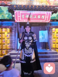 《杨柳青古巷遇戎装赋》
 
暮临津沽杨柳青墟，长街灯华，古肆连楹。余闲步漫游，忽见一戎装少年立巷隅，玄铠鎏纹，长戈倚侧，眉目疏朗，英气凌云。金甲映霓虹，身姿挺拔若青松临风，顾盼之间，俊采飞扬，令人目移心喜。
 
余趋前相与语，言欲留影纪此相逢。少年温雅谦和，闻言欣然颔首，俯仰立坐，皆顺人意，摆姿展态，毫无倦怠，待人以诚，气度温润，初见便觉心头烦扰消解大半。方调镜头之际，一家四口缓步而至，远客夫妻携两稚子，远道来游古镇。夫君执机欲为妻取景，持镜茫然，不知章法。余侧立旁，细教取景光影、身形站位之法，嘱其寻温柔姿态衬佳人风姿。
 
其夫闻言莞尔，回身笑语妻曰：“无妨，可依偎相拥，随心喜乐，不必拘谨。”语罢伸手相挽，妻霎时展颜，笑靥如花，眉眼间羞怯尽散。身旁两童见状，亦拍手嬉闹，绕膝奔走，满是童真烂漫。少顷夫君移步上前，自请立镜前，摹美猴王腾跃之姿，抬手探额，嬉闹无拘，阖家笑语充盈古巷。
 
余立旁静观，心下慨然。此一家四口，夫知惜妻，妻善解意，稚童无忧，彼此体恤成全，无隔阂拘束，方是华夏家庭本真之温情。尘世奔波，世人常困于疏离、苛责，心有郁结，难寻松弛暖意。今古镇灯火、飒爽少年治愈尘俗疲惫，更得此和睦阖家涤荡心绪，恍然知晓治愈本心者，从非远在山海，乃是人间相守的松弛与包容。
 
戎装少年以谦和待人，予过客温柔；寻常夫妇以坦诚相待，予彼此欢愉。烟火古巷，铠甲英姿衬阖家温情，一静一动，皆是人间至善光景。愿九州万户皆如此：夫妻相知不藏拘谨，亲子相伴常存欢颜，家人之间随心抒意，彼此成全，相守和乐，岁岁常有笑语相伴，岁岁皆得温柔治愈。世间万千烦忧，皆可在家人松弛暖意里缓缓消融，人间至幸，莫过于阖家自在，心无芥蒂，喜乐常随。配图