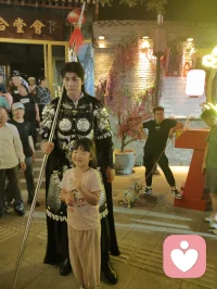 《杨柳青古巷遇戎装赋》
 
暮临津沽杨柳青墟，长街灯华，古肆连楹。余闲步漫游，忽见一戎装少年立巷隅，玄铠鎏纹，长戈倚侧，眉目疏朗，英气凌云。金甲映霓虹，身姿挺拔若青松临风，顾盼之间，俊采飞扬，令人目移心喜。
 
余趋前相与语，言欲留影纪此相逢。少年温雅谦和，闻言欣然颔首，俯仰立坐，皆顺人意，摆姿展态，毫无倦怠，待人以诚，气度温润，初见便觉心头烦扰消解大半。方调镜头之际，一家四口缓步而至，远客夫妻携两稚子，远道来游古镇。夫君执机欲为妻取景，持镜茫然，不知章法。余侧立旁，细教取景光影、身形站位之法，嘱其寻温柔姿态衬佳人风姿。
 
其夫闻言莞尔，回身笑语妻曰：“无妨，可依偎相拥，随心喜乐，不必拘谨。”语罢伸手相挽，妻霎时展颜，笑靥如花，眉眼间羞怯尽散。身旁两童见状，亦拍手嬉闹，绕膝奔走，满是童真烂漫。少顷夫君移步上前，自请立镜前，摹美猴王腾跃之姿，抬手探额，嬉闹无拘，阖家笑语充盈古巷。
 
余立旁静观，心下慨然。此一家四口，夫知惜妻，妻善解意，稚童无忧，彼此体恤成全，无隔阂拘束，方是华夏家庭本真之温情。尘世奔波，世人常困于疏离、苛责，心有郁结，难寻松弛暖意。今古镇灯火、飒爽少年治愈尘俗疲惫，更得此和睦阖家涤荡心绪，恍然知晓治愈本心者，从非远在山海，乃是人间相守的松弛与包容。
 
戎装少年以谦和待人，予过客温柔；寻常夫妇以坦诚相待，予彼此欢愉。烟火古巷，铠甲英姿衬阖家温情，一静一动，皆是人间至善光景。愿九州万户皆如此：夫妻相知不藏拘谨，亲子相伴常存欢颜，家人之间随心抒意，彼此成全，相守和乐，岁岁常有笑语相伴，岁岁皆得温柔治愈。世间万千烦忧，皆可在家人松弛暖意里缓缓消融，人间至幸，莫过于阖家自在，心无芥蒂，喜乐常随。配图
