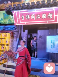 柳青古巷观群伶赋！
津沽之西，杨柳青墟，华灯千叠，古肆纵横。余夜踏长街，入汉服雅馆，见诸伶衣袂纷纭，百态纷呈，恍若穿越千年京华。
有宫娥红罗曳地，步缓腰柔；萨满彩衣缀饰，古韵苍然；财神锦袍鎏金，笑意温厚；龙袍帝者端立，却无半分矜傲。余趋前请其展姿，帝王欣然舒袖，执扇斜倚，俯仰随吾心意，平易可亲，全无居高之态；八戒扮相憨然敦厚，待人温和，观之使人忘忧。
更有一舞姬，素袖翻飞，身轻似燕，踏光旋舞，一颦一动皆藏风月。余伫立观舞，尘心烦扰尽数消散，心旷神怡，文思奔涌，倚兴挥毫，顷刻成赋，递与佳人。彼展卷细读，眼含温柔，浅笑揖别，眉眼盈盈，相逢之喜，溢于眉宇，此乐难言，美哉甚哉。
 
余素怀三境之心：持儒者赏美之温，怀释者渡人之善，存道者随性之旷，恰似柳七流连市井，不束于俗规，乐于观人间风月、赏众生清妍。世间多困于自我内耗，鲜少静心欣赏旁人光彩，殊不知赞美本是双向治愈。予人一眼欣赏，赠人一纸诗文，一份赤诚欢喜流转彼此心间，愁绪自消，暖意自生。
此间伶人各有风姿，不掩各自本真；往来游人各怀心事，皆可借古巷风情抚平褶皱。帝王放下威仪，舞姬舒展柔姿，财神藏起世俗功利，戏偶褪去扮演隔阂，人人卸下紧绷防备，松弛自在，便是人间最好疗愈。
不必高居庙堂寻清欢，不必遁入深山求心安，市井灯火、衣袂翩跹、相逢一笑、提笔成篇，皆是治愈良方。以坦荡心赏世间美，以温柔意传人间爱，随遇而安，随性抒怀，儒释道相融于心，在烟火长巷中寻得自在真我，把细碎欢喜赠予相逢之人，便是此生通透洒脱。配图