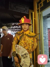 柳青古巷观群伶赋！
津沽之西，杨柳青墟，华灯千叠，古肆纵横。余夜踏长街，入汉服雅馆，见诸伶衣袂纷纭，百态纷呈，恍若穿越千年京华。
有宫娥红罗曳地，步缓腰柔；萨满彩衣缀饰，古韵苍然；财神锦袍鎏金，笑意温厚；龙袍帝者端立，却无半分矜傲。余趋前请其展姿，帝王欣然舒袖，执扇斜倚，俯仰随吾心意，平易可亲，全无居高之态；八戒扮相憨然敦厚，待人温和，观之使人忘忧。
更有一舞姬，素袖翻飞，身轻似燕，踏光旋舞，一颦一动皆藏风月。余伫立观舞，尘心烦扰尽数消散，心旷神怡，文思奔涌，倚兴挥毫，顷刻成赋，递与佳人。彼展卷细读，眼含温柔，浅笑揖别，眉眼盈盈，相逢之喜，溢于眉宇，此乐难言，美哉甚哉。
 
余素怀三境之心：持儒者赏美之温，怀释者渡人之善，存道者随性之旷，恰似柳七流连市井，不束于俗规，乐于观人间风月、赏众生清妍。世间多困于自我内耗，鲜少静心欣赏旁人光彩，殊不知赞美本是双向治愈。予人一眼欣赏，赠人一纸诗文，一份赤诚欢喜流转彼此心间，愁绪自消，暖意自生。
此间伶人各有风姿，不掩各自本真；往来游人各怀心事，皆可借古巷风情抚平褶皱。帝王放下威仪，舞姬舒展柔姿，财神藏起世俗功利，戏偶褪去扮演隔阂，人人卸下紧绷防备，松弛自在，便是人间最好疗愈。
不必高居庙堂寻清欢，不必遁入深山求心安，市井灯火、衣袂翩跹、相逢一笑、提笔成篇，皆是治愈良方。以坦荡心赏世间美，以温柔意传人间爱，随遇而安，随性抒怀，儒释道相融于心，在烟火长巷中寻得自在真我，把细碎欢喜赠予相逢之人，便是此生通透洒脱。配图