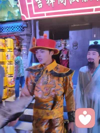 柳青古巷观群伶赋！
津沽之西，杨柳青墟，华灯千叠，古肆纵横。余夜踏长街，入汉服雅馆，见诸伶衣袂纷纭，百态纷呈，恍若穿越千年京华。
有宫娥红罗曳地，步缓腰柔；萨满彩衣缀饰，古韵苍然；财神锦袍鎏金，笑意温厚；龙袍帝者端立，却无半分矜傲。余趋前请其展姿，帝王欣然舒袖，执扇斜倚，俯仰随吾心意，平易可亲，全无居高之态；八戒扮相憨然敦厚，待人温和，观之使人忘忧。
更有一舞姬，素袖翻飞，身轻似燕，踏光旋舞，一颦一动皆藏风月。余伫立观舞，尘心烦扰尽数消散，心旷神怡，文思奔涌，倚兴挥毫，顷刻成赋，递与佳人。彼展卷细读，眼含温柔，浅笑揖别，眉眼盈盈，相逢之喜，溢于眉宇，此乐难言，美哉甚哉。
 
余素怀三境之心：持儒者赏美之温，怀释者渡人之善，存道者随性之旷，恰似柳七流连市井，不束于俗规，乐于观人间风月、赏众生清妍。世间多困于自我内耗，鲜少静心欣赏旁人光彩，殊不知赞美本是双向治愈。予人一眼欣赏，赠人一纸诗文，一份赤诚欢喜流转彼此心间，愁绪自消，暖意自生。
此间伶人各有风姿，不掩各自本真；往来游人各怀心事，皆可借古巷风情抚平褶皱。帝王放下威仪，舞姬舒展柔姿，财神藏起世俗功利，戏偶褪去扮演隔阂，人人卸下紧绷防备，松弛自在，便是人间最好疗愈。
不必高居庙堂寻清欢，不必遁入深山求心安，市井灯火、衣袂翩跹、相逢一笑、提笔成篇，皆是治愈良方。以坦荡心赏世间美，以温柔意传人间爱，随遇而安，随性抒怀，儒释道相融于心，在烟火长巷中寻得自在真我，把细碎欢喜赠予相逢之人，便是此生通透洒脱。配图
