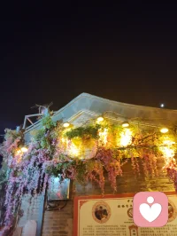 古巷香韵风物赋！
 
津沽杨柳青长街，夜色铺陈，百家风物分列檐下。有戏曲冠冕绮丽敷彩，香肆悬“天佑合香”匾额，古法香囊满架垂芳，瑞狮摆件藏民俗喜气，木牌箴言静立门扉，繁花灯影缀满檐角。
 
观诸风物：凤冠珠翠层叠，映红光而蕴雅致；合香囊纳草木清芬，一嗅便涤荡尘浊；木牌镌素简哲语，字句温润安抚心绪；瑞狮藏市井吉意，艳色消人沉郁。一街之间，声色香韵俱全，目之所遇皆民俗温柔，鼻之所闻皆草木清宁。
 
心理学云，多感官治愈最能疏解内耗。目赏绮丽冠饰、暖巷灯火，鼻纳天然古香，心品简约箴言，多重温和感知层层包裹心神。平日缠身的焦虑紧绷，随香气漫散、风物入眼缓缓消融。不必寻深山静境，此巷烟火器物，便是安放烦忧的疗愈之所。
 
洛神以仙姿慰人眼目，古巷以百味风物安人心魂。制香者守古法以传清宁，造物者雕器物以寄祥和，一字一香一饰，皆藏抚慰人心的力量。踏过这条缀满繁花与古物的街巷，俗世褶皱尽数舒展，只留一身清宁，满心温柔。配图