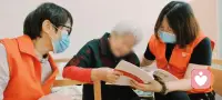 用乡音温暖时光
周日的暖冬，我穿过半座城市——从龙岗到宝安，赴一场温暖的约定。在长者服务中心，预备会刚结束，我与王姐姐就在一楼大厅遇见了正看电视的叶奶奶。

“上次那个女孩怎么没来呀？”她一见我们便问，语气里带着些许牵挂。

我笑着用客家话回应：“阿婆，我哋今日来陪汝。”熟悉的乡音像一把钥匙，瞬间点亮了奶奶的眼睛。她亲切地握住我们的手：“汝们好有心啊！”随后，热情地将我们引向她那间温馨的房间。那一刻，时光仿佛也放慢了脚步。

房间里，我们仨静静围坐在白发长者身旁。我坐在奶奶的床沿，背心上“爱与陪伴”的字样，无声地诉说着此刻流动的温情。这不仅仅是一次探望，更是一场用最熟悉的乡音——客家话，展开的心灵对话。

我们轻轻翻动歌本。“汝爱唱麦感歌？”我用客家话问。奶奶的歌声随即响起，《北京的金山上》《夫妻双双把家还》……一首接一首。她唱得投入，嘴角不时漾开笑意，那是一种被深深懂得的欣慰。她告诉我们，阿公在世时常说她只会讲客家话，可有趣的是，她唱起普通话歌曲却字正腔圆。

她还拿出一本珍藏的《中外歌曲300首》，说是当老师的阿公留下的宝贝。问起跟谁学的唱歌，她颇为自豪：“自学的。”真让人敬佩！乡音与旋律交织，近一个小时的时光在歌声中悄然流淌。听说活动快结束了，奶奶起身活动，说腰有些疼。我陪她一起缓缓扭腰，听她说自己每天五点多就起来运动，“要多动动，身体才会好”。

临别时，我轻轻拥抱她：“谢谢您陪我，要乖乖的哈。”奶奶紧握我们的手，依依不舍：“多谢你们，这么有心来陪我聊天。”

“爱与陪伴”的精髓，就藏在这些细碎的时光里。在这里，每一句客家话的问候，每一段用乡音唱起的歌谣，都在轻轻诉说：无论岁月如何流转，您从未被遗忘。您的乡音、您的记忆、您的情感，始终有人愿意倾听、渴望理解。

这便是“爱与陪伴”为长者们筑起的温暖港湾——用一句乡音，温柔一段漫长的时光。

写在后记：
我看见的老人
在她的神情里，我看见了失落后的期待，孤独中被点燃的热情，以及对生活与歌唱不变的热爱与坚持，最终都化为离别时满满的不舍。

看见的看见
当老人流露出失落时，我思考着如何陪伴。所幸，共同的乡音成为我们之间最自然的桥梁。我们用客家话共情，用音乐沟通，在歌声中达到同频共振。我也看见了自己的不足——会唱的歌太少了。若有时间，我定会再来陪伴，也多学一些歌，让下一次的共振更加响亮。配图